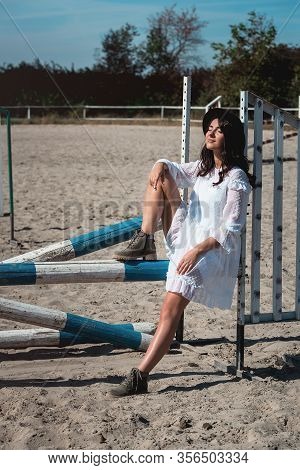 Beautiful Sexy Girl Posing On The Horizontal Crosspiece On A Horse Epodrom. Female Wearing White Dre
