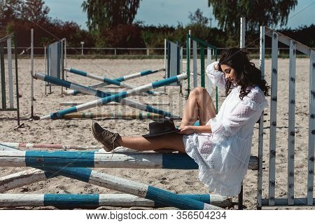 Beautiful Sexy Girl Posing On The Horizontal Crosspiece On A Horse Epodrom. Female Wearing White Dre