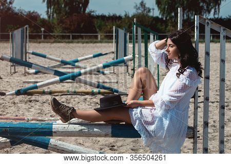 Beautiful Sexy Girl Posing On The Horizontal Crosspiece On A Horse Epodrom. Female Wearing White Dre