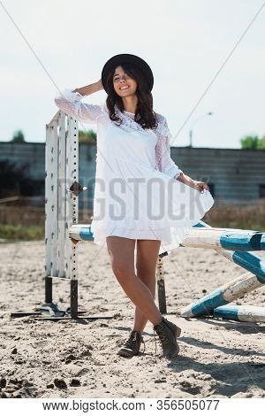 Beautiful Sexy Girl Posing On The Horizontal Crosspiece On A Horse Epodrom. Female Wearing White Dre