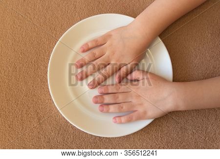 Childrens Little Hands Lie In An Empty White Plate On The Table