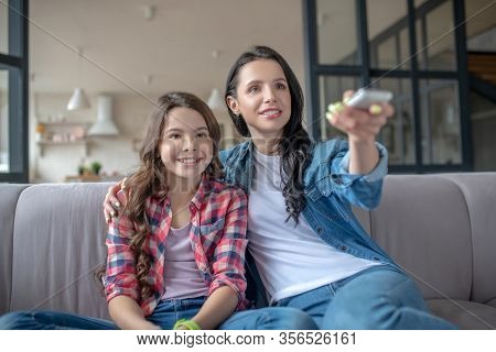Mom And Her Daughter Sitting Next To Each Other And Watching Tv