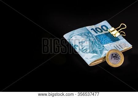 One Hundred Reais Bank Notes And One Reais Coin, Brazilian Money On Isolated Black Background. Brazi