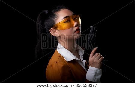 Portrait Beautiful Asea Woman Wearing A Yellow Suit One Hand Holding Pistol Gun At The Black Backgro