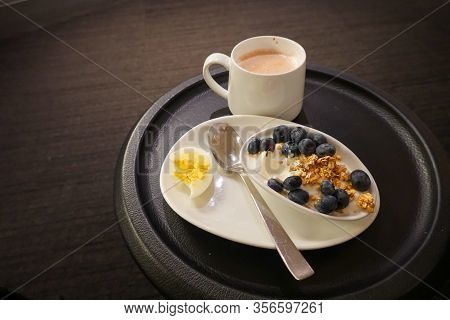 A Breakfast Snack Of An Hardboiled Egg, Yogurt, Blueberries And Cappuccino At An Airport Lounge.