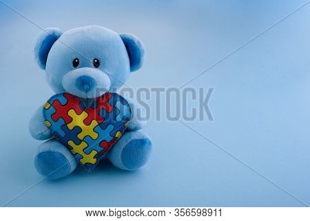 World Autism Awareness, Concept With Teddy Bear Holding Puzzle Or Jigsaw Pattern On Heart On Blue Ba