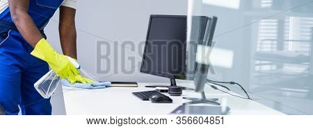 Young Male Maid Cleaning Glass Desk With Feather Duster In Office