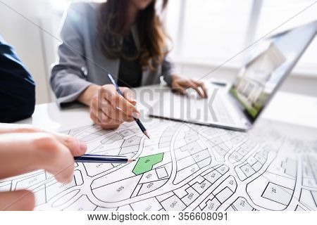 Two People Looking At Cadastre Map With Laptop On Desk