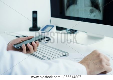 closeup of a young doctor man, wearing a white coat, sitting at his desk checking a chest radiograph in his computer