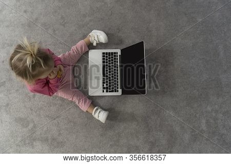 Small Cute Blond Caucasian Baby Laying On Floor On Grey Rug And Watching Cartoons On Laptop With Gre