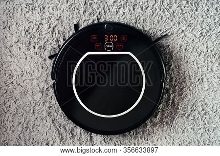 Automatic Robot Vacuum Cleaner In Black On A Gray Shag Carpet. New Modern Technologies For Apartment
