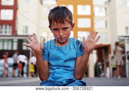 A Little Boy Sits On The Ground With His Hands Up And Protests. The Concept Of Raising A Difficult N