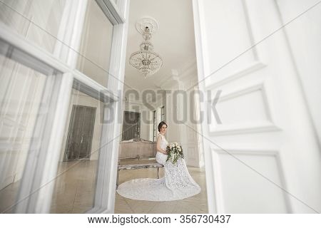 Beautiful Bride Posing In Wedding Dress In A White Photo Studio. Mirror. Sofa. Bouquet. The Door. Ch