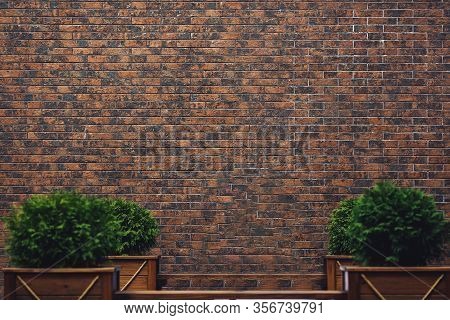 Background Wall Of Dark Brown Clinker Bricks And Wooden Benches With Flower Beds. Copy Space