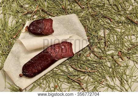 Dried Sausage Made Of Roe Deer Meat. Cut With Slices On Parchment. Flooring Made Of Pine Needles.