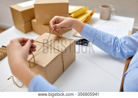delivery, mail service, people and shipment concept - close up of woman packing eco parcel box and tying rope at post office