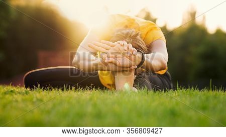 Young Attractive Woman Practicing Yoga In The Park At Sunset. Outdoor Sport Activity. Practice Yoga 