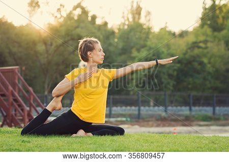 Young Attractive Woman Practicing Yoga In The Park At Sunset. Outdoor Sport Activity. Practice Yoga 