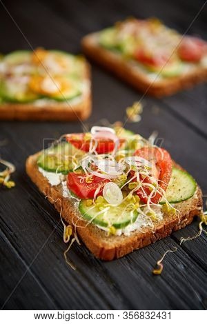 Healthy vege toasts with onion, cucomber, cherry tomatoes, crumbled feta cheese and radish sprouts. Table top view on black wooden background