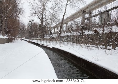 Urban Stream In Winter. The Lybid River (kyiv, Ukraine) In The Snow. Elevated Pipeline Near The Rive
