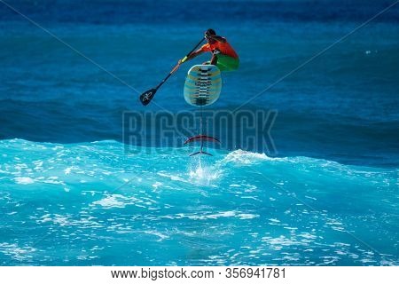OAHU, HI / USA - DECEMBER 01, 2018: Surfer jumps on a hydrofoil surfboard and shows the fins