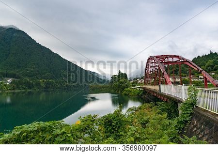 Red Bridge And River In The Mountain Valley. Japanese Countryside Landscape. Atera Valley In Kiso Va