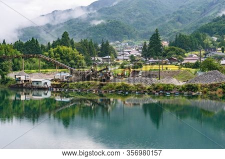 Open Quarry Pit With Piles Of Sand And Gravel On The River Bank With Mountains On The Background. Ja