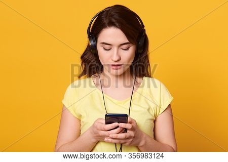 Image Of Brunette Serious Woman Wearing Casual Clothing, Listening To Music On Smartphone Via Earpho