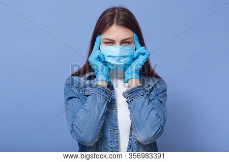 Studio Portrait Of Young Brunette Girl Having Headache, Holding Hands On Temples, Wearing Medical Fl