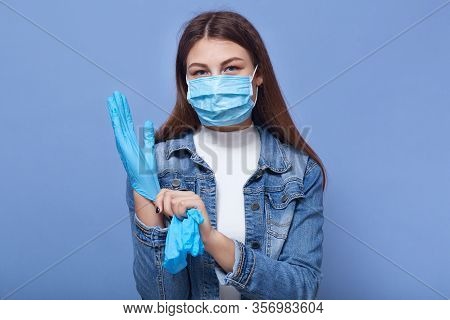 Studio Shot Of Female Posing Isoalted Over Blue Background, Young Woman Putting On Blue Disposable L