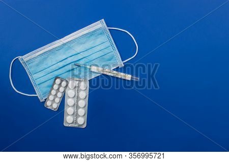 White Medicine Blister Packs Pills, Thermometer, Medical Face Mask Flat Lay On Colorful Blue Backgro