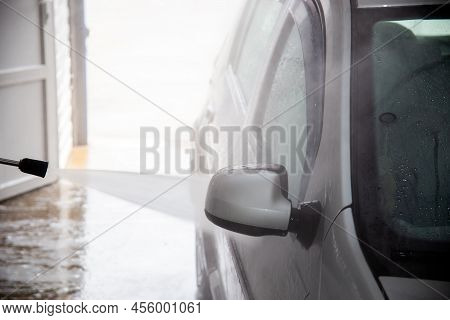 A Process Of Flushing Soap Sud On Silver Car Mirror With Pressurised Water Stream At Self-service In