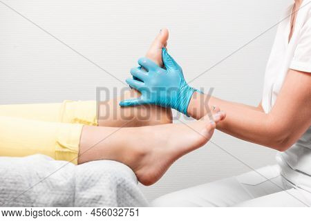 A Chiropodist Massages The Feet Of Client. Close-up Of Legs And Master's Hands In Blue Medical Glove