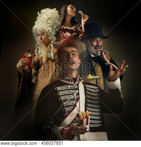 Medieval People As Royalty Persons In Vintage Clothing Eating Fast Food, Fries On Dark Background. C