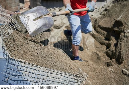 Close Up Of Man With Shovel In His Hands Throwing Cementitious Floor Screed Material Into Container 