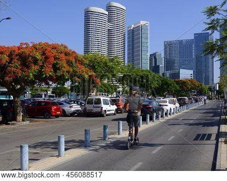 Tel Aviv. Israel. June 2022. A Man Rides An Electric Scooter. In The Background Are Skyscrapers, A B