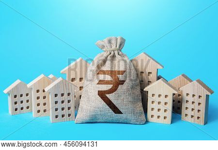 Indian Rupee Money Bag Among Town Houses Figurines. Realtor Services. Sale Of Real Estate. Property 