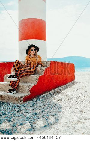 Gorgeous Fashionable Woman Posing While Sitting On A Lighthouse. Summer Photo Of A Girl In A Yellow-