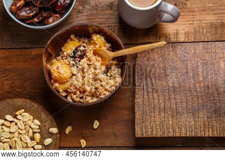 A Plate Of Couscous With Saffron And Nuts On A Wooden Table Next To Dates And A Jug Of Fruit Broth. 