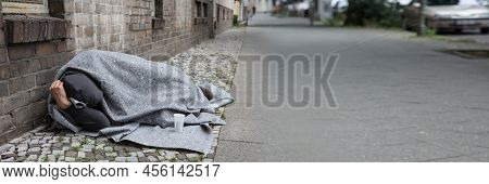 Homeless Man Covered With Blanket Sleeping On Street In City