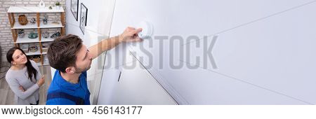 Pretty Woman Standing Near Repairman Installing Smoke Detector On Wall At Home