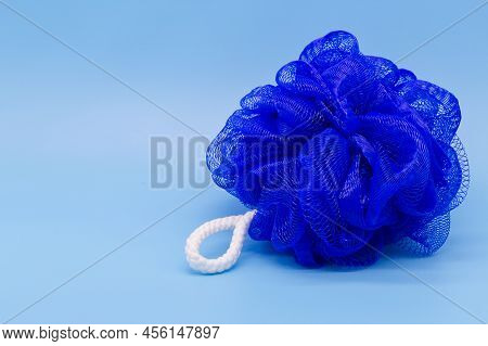 Blue Mesh Pouf Bath Sponge Washcloth Single Object On Blue Background Closeup Photo With Copy Space.