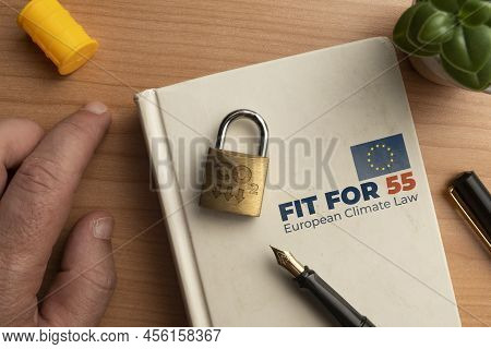 Fit For 55 European Climate Law Concept: A Book On A Wooden Table With A Man Hand A Lock And A Pen