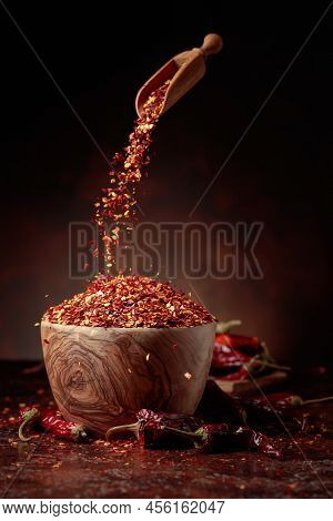 Chilli Flakes Are Poured Into A Wooden Dish. Chilli Flakes And Dried Chili Peppers On A Brown Backgr