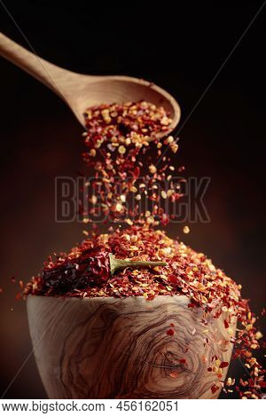 Chilli Flakes Are Poured Into A Wooden Dish. Chilli Flakes And Dried Chili Peppers On A Brown Backgr