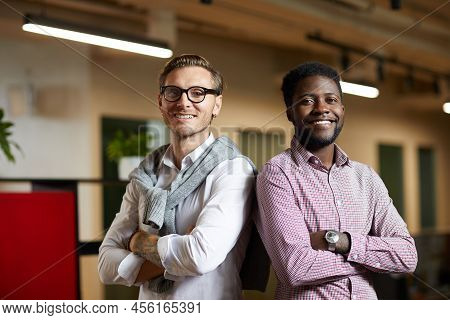Positive Confident Young Multi-ethnic Startuppers Standing Back To Back And Looking At Camera In Off