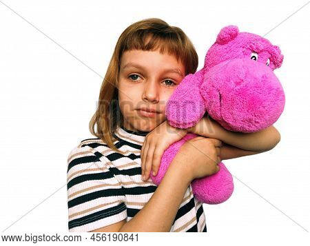 A Cute Caucasian Girl Of 7 Years Old With Blond Hair Cuddles And Hugs A Pink Hippopotamus. Hippo Plu