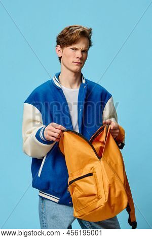 A Joyful Student In A Fashionable Bomber Jacket Stands With An Open Orange Backpack In His Hands On 