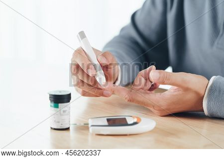 Asian Man Using Lancet On Finger For Checking Blood Sugar Level By Glucose Meter, Healthcare And Med