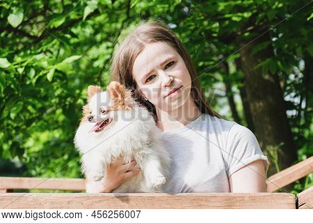 Young Woman With Long Straight Hair And Fluffy Small Dog For Walk In Park